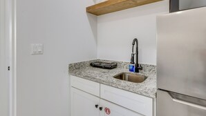 A kitchen with a stainless steel refrigerator, a granite countertop, a sink, and a wooden shelf above the countertop. - Groups Welcome! SPI Studio on Multi-unit Property (South Padre Island)