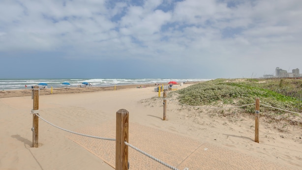 Ein Sandstrand mit Holzzaun und Seilabsperrung, der zum Meer führt.