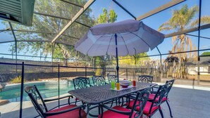 Een terras buiten met een zwembad, omringd door metalen stoelen en een tafel met een parasol.