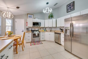 A modern kitchen with white cabinets, stainless steel appliances, and a dining area with a table and chairs. - Resort-style Pool & Yard: Luxe Duplex Near Disney! (Davenport)
