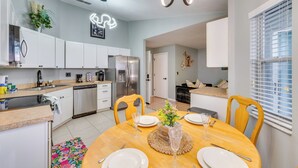 Een moderne keuken met witte kasten, roestvrijstalen apparatuur en een eethoek met een houten tafel gedekt voor vier personen.