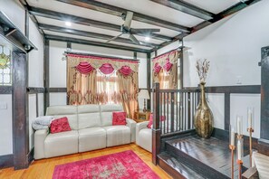 A living room with a white sofa, red cushions, a wooden floor, a red rug, a ceiling fan, and a staircase with a vase and candles. - Walkable Schenectady Getaway: 2-unit Campus Hub (Schenectady)