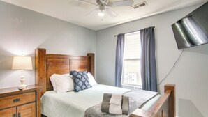 A bedroom with a wooden bed frame, a nightstand with a lamp, a flat-screen TV mounted on the wall, and a window with curtains. - 3 Mi to Branson Strip: 2-unit Gem w/ Pool Access! (Branson)