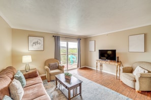 Ein Wohnzimmer mit einer Couch, Sesseln, einem Couchtisch, einem Fernseher und einem Balkon mit Aussicht.