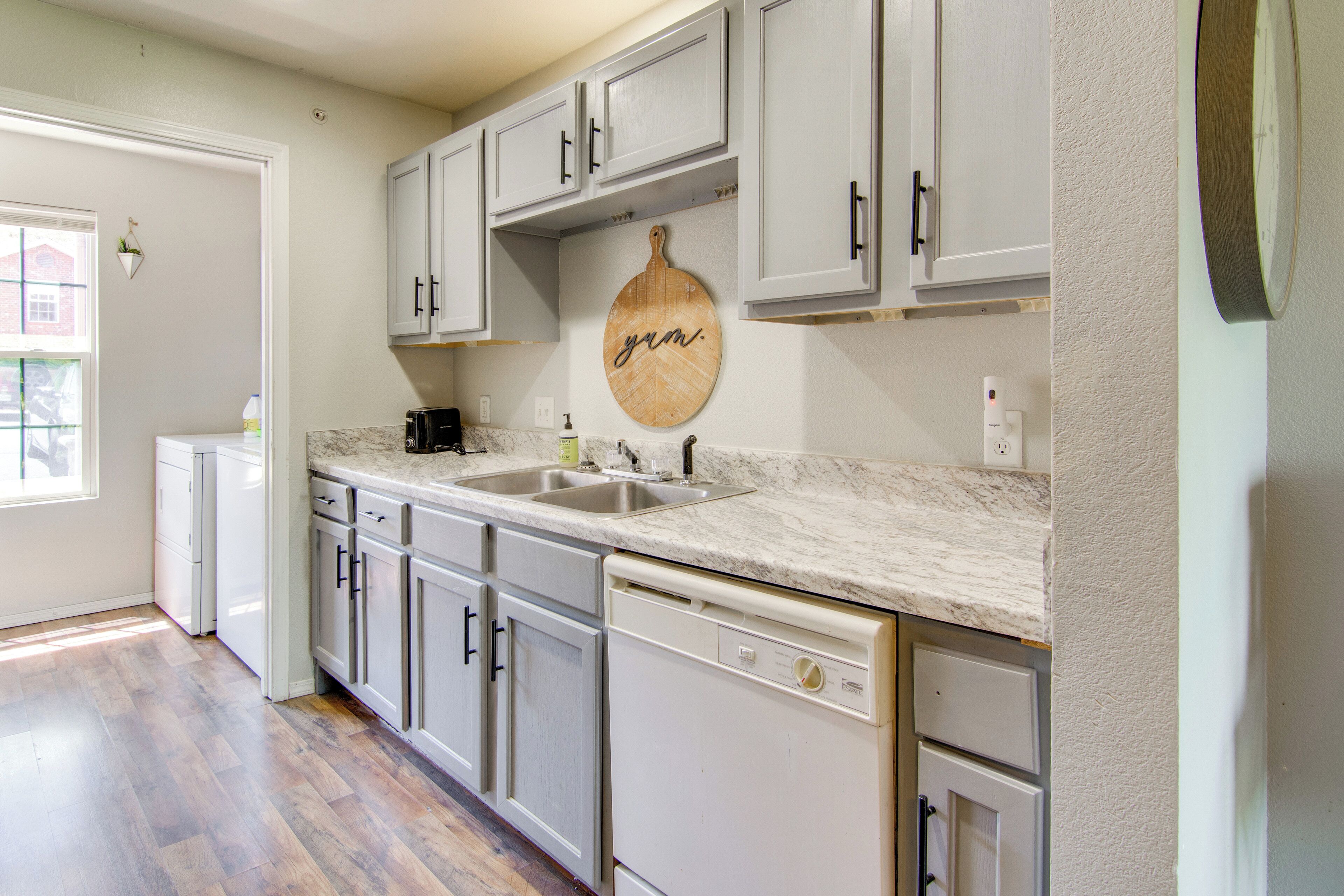 A kitchen with white cabinets, a marble countertop, and a wooden cutting board with "grm" written on it.
