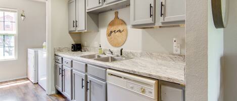 A kitchen with white cabinets, a marble countertop, and a wooden cutting board with "grm" written on it.