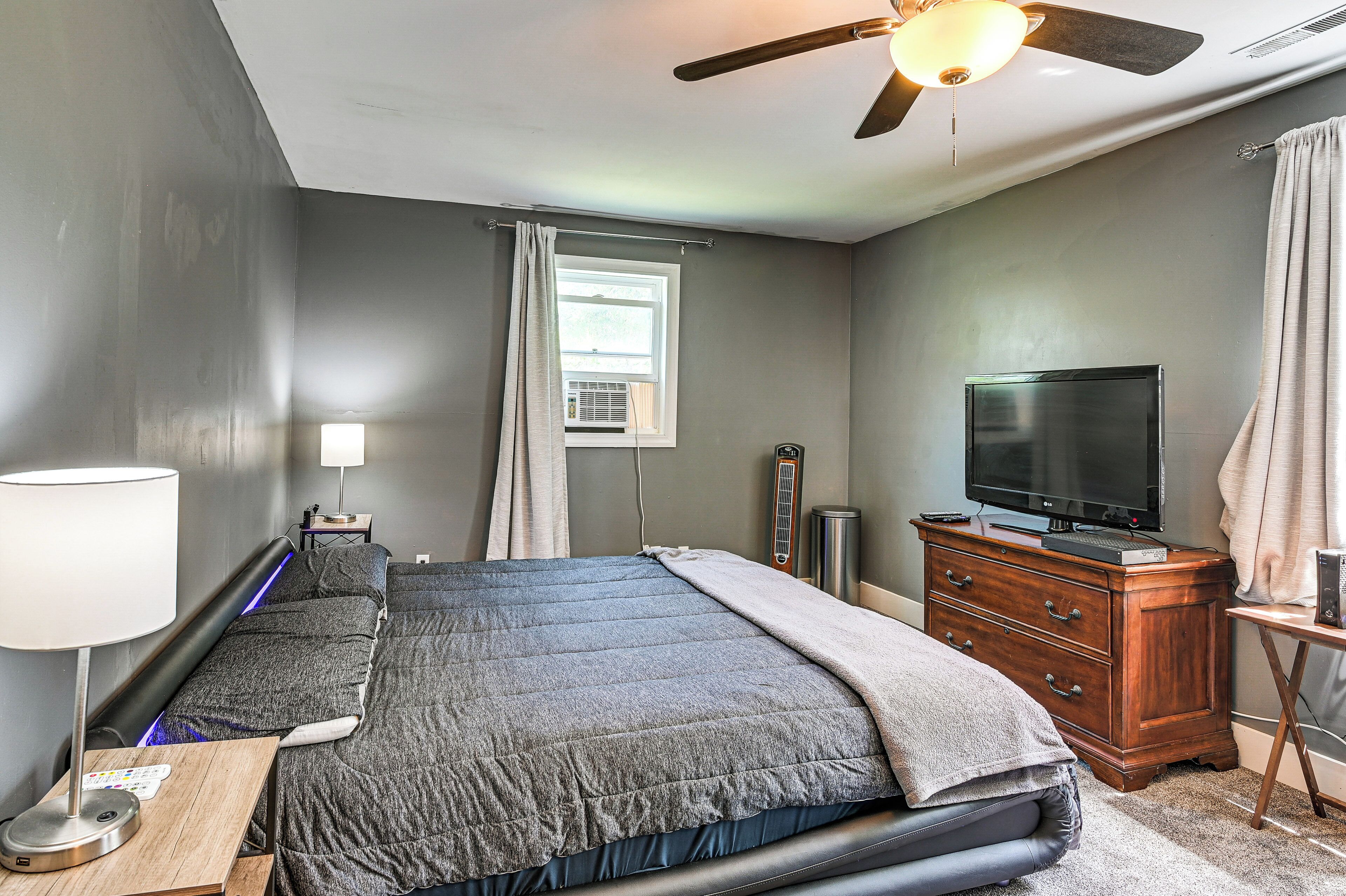 Ein Schlafzimmer mit Bett, Schreibtisch, Fernseher, Deckenventilator und Fenster.