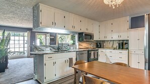 A kitchen with white cabinets, a marble countertop, a wooden dining table, and a chandelier. - 2 Mi to Myrtle Beach Boardwalk: 2 King Beds! (Myrtle Beach)
