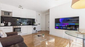 Cozinha moderna com micro-ondas, forno e máquina de lavar roupa, uma mesa de centro de vidro e uma TV exibindo uma interface de rede.