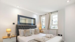Quarto com cama grande, luminárias de cabeceira, espelho e janela com cortinas.