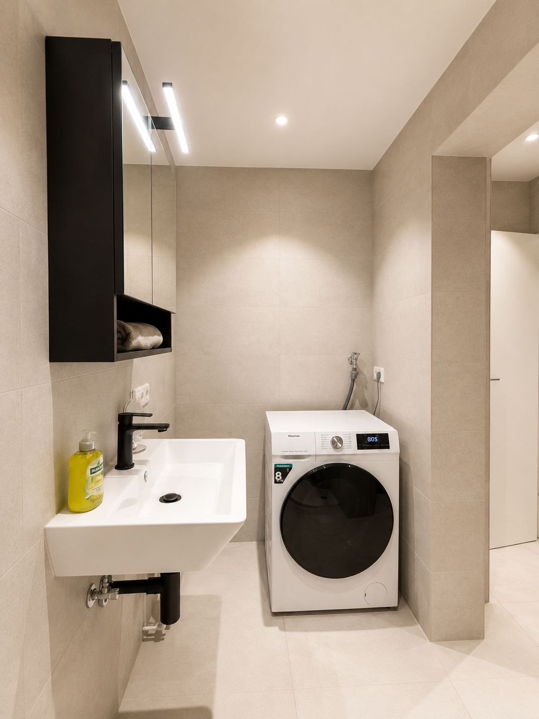 Une salle de bain moderne équipée d’un lavabo, d’un miroir et d’un lave-linge encastré.