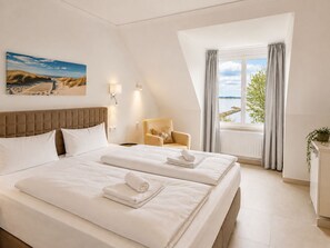 A hotel room with two beds, a view of the sea, a painting on the wall, and a chair. - Oceanview Residences Lauterbach Rügen (Putbus)