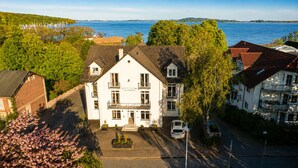 A white building with a balcony, a car parked in front, and a view of the sea.