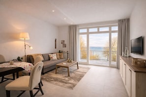 A modern living room with a sofa, coffee table, TV, and a dining area with a table and chairs. - Oceanview Residences Lauterbach Rügen (Putbus)
