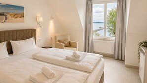 A bedroom with a large bed, a chair, a window with curtains, and a painting on the wall.