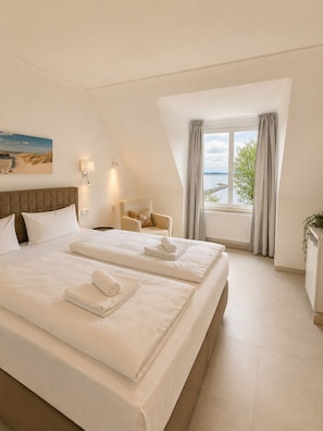 Un dormitorio con una cama grande, una silla, una ventana con cortinas y un cuadro en la pared.