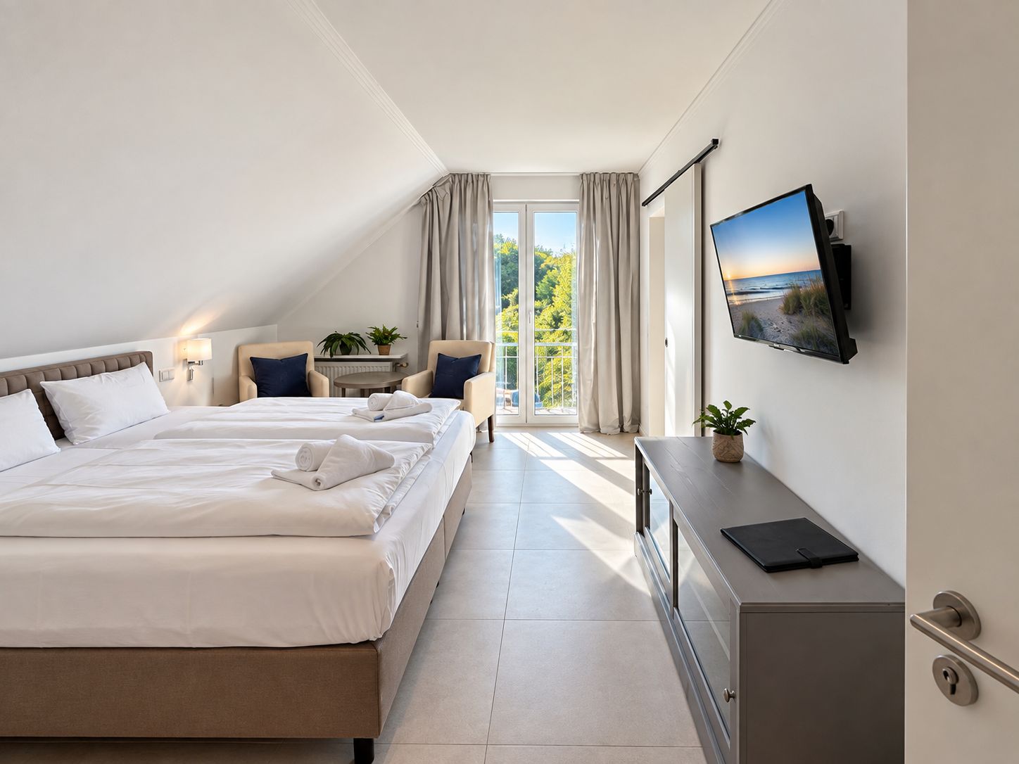 Ein Hotelzimmer mit einem großen Bett, einem Schreibtisch, einem Fernseher und einem Balkon mit Vorhängen.