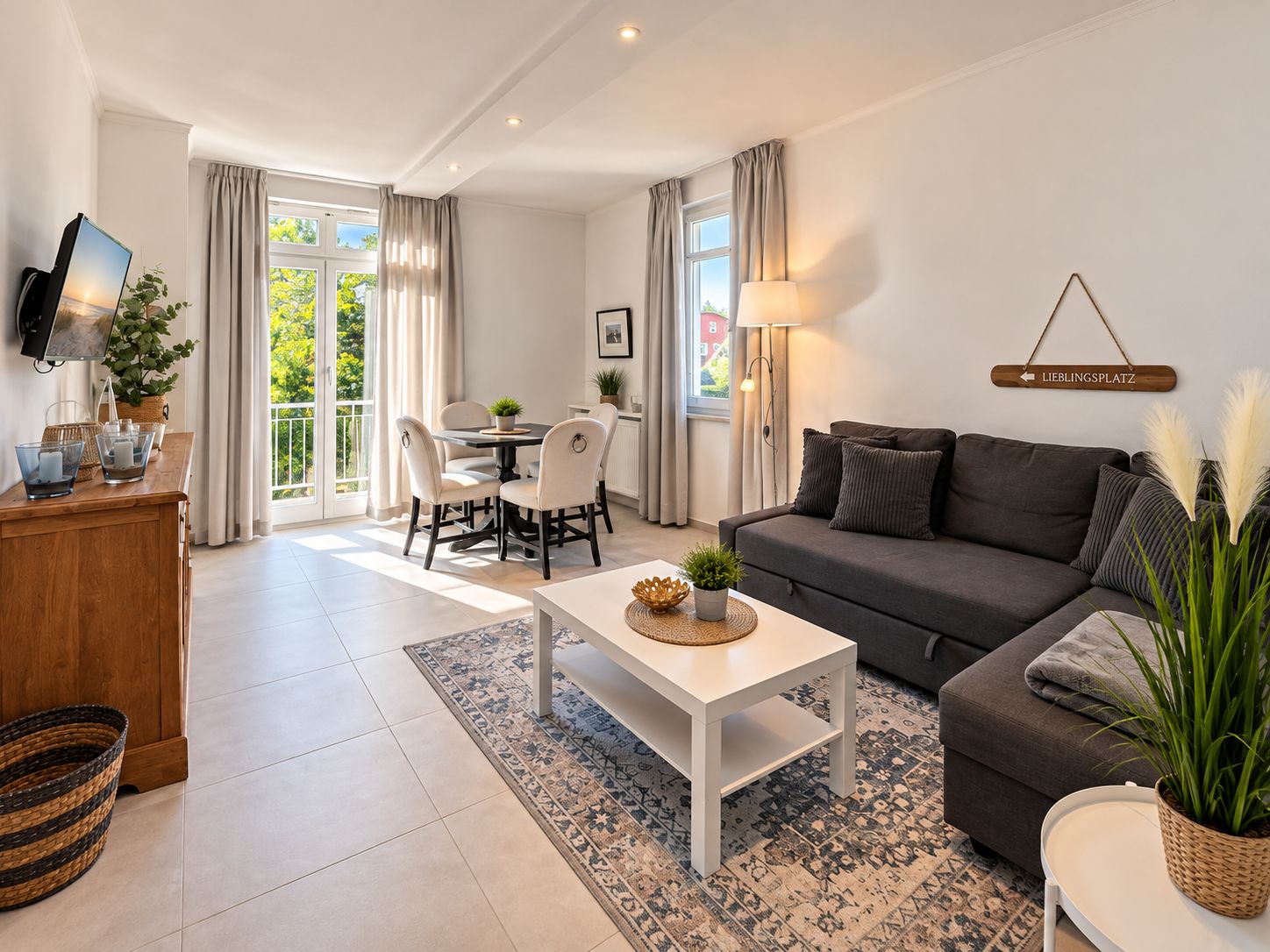 Ein modernes Wohnzimmer mit einer Couch, einem Esstisch mit Stühlen, einem an der Wand befestigten Fernseher und einem Schild mit der Wegbeschreibung.