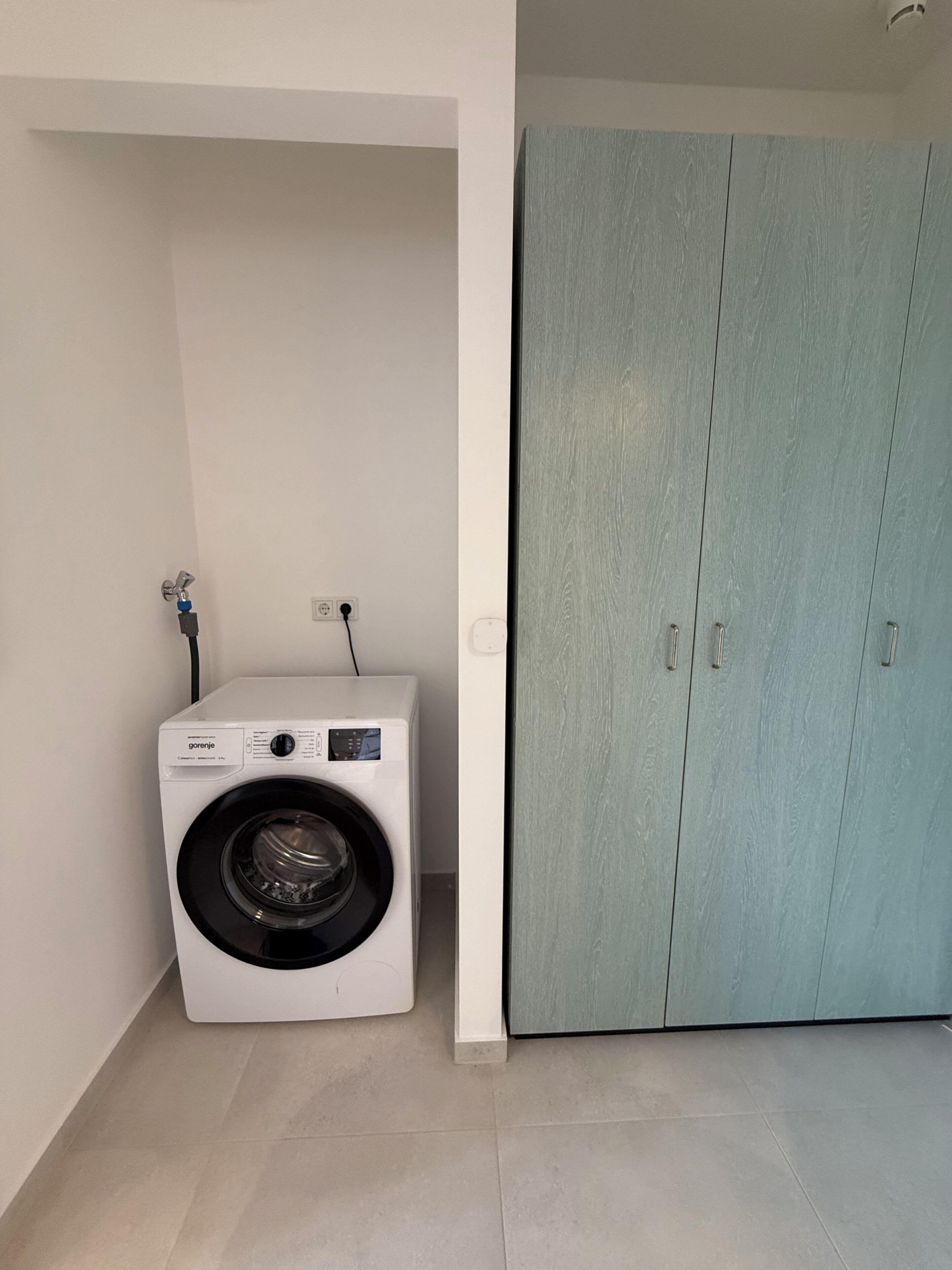A compact room with a washing machine, a wardrobe, and a tiled floor.