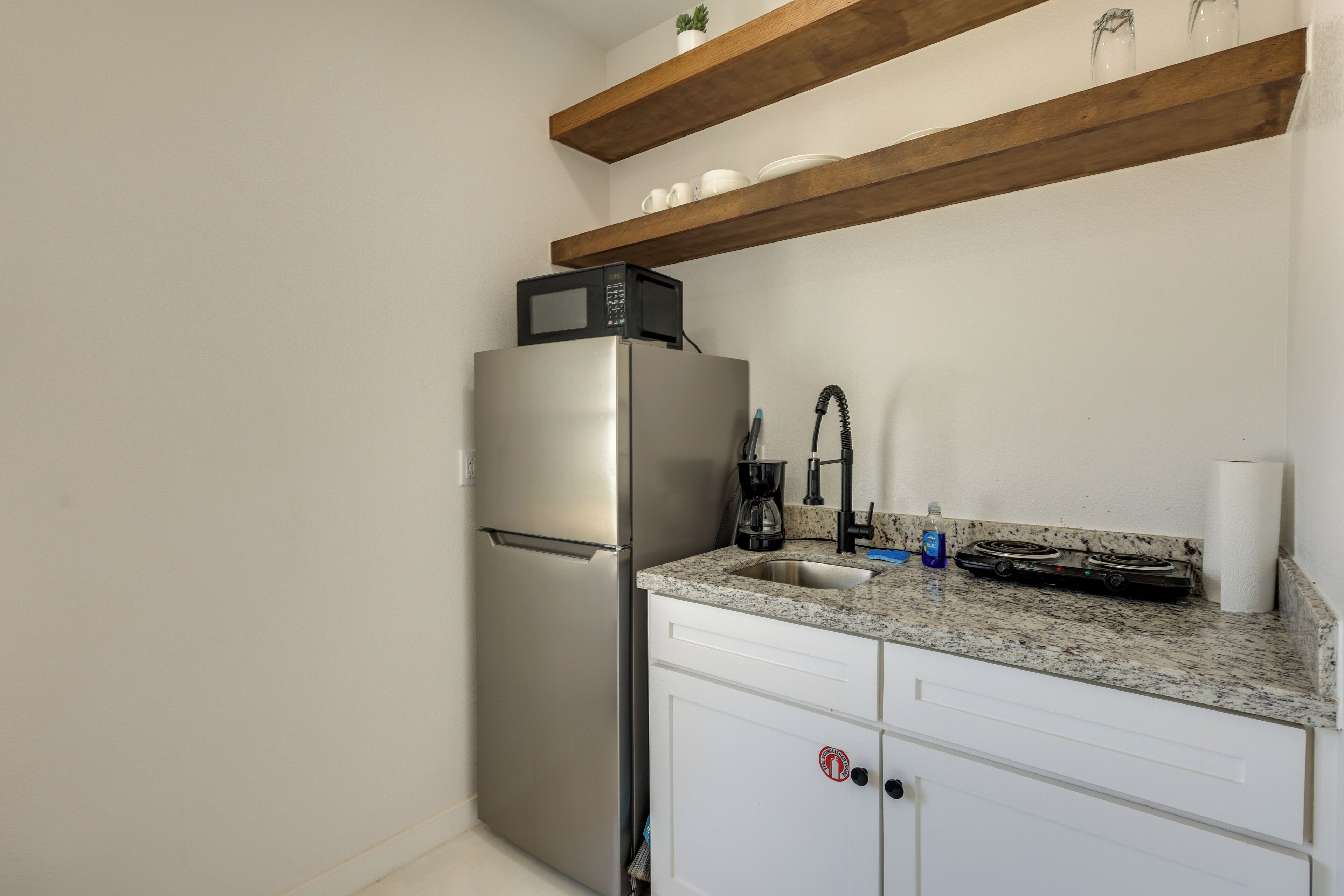 A compact kitchen with a stainless steel refrigerator, a microwave, a sink, and a stove.