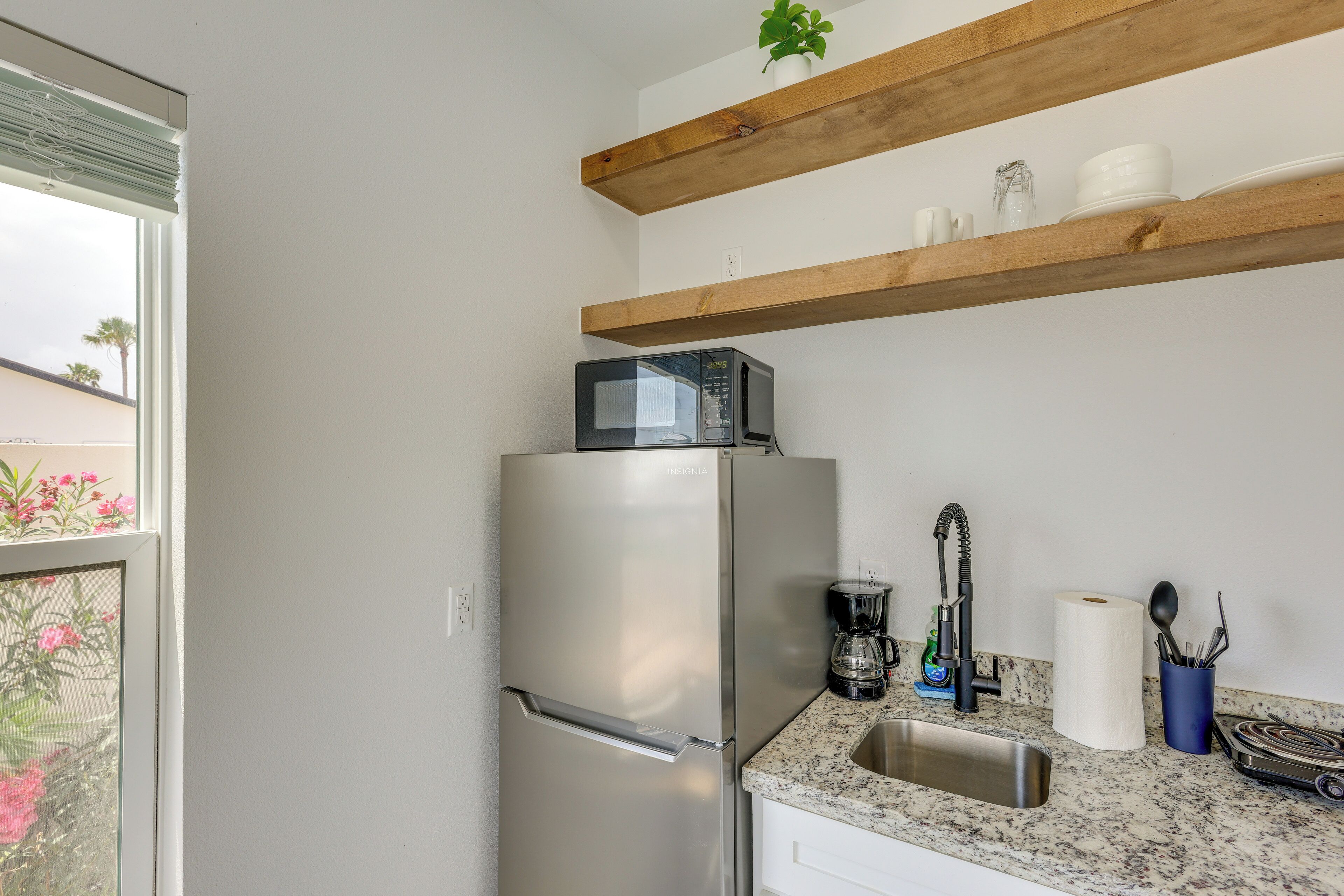 A kitchen with a stainless steel refrigerator, a sink, a coffee maker, and a wooden shelf above the counter.