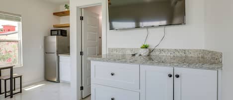 A modern kitchen with a flat-screen TV, white cabinets, and a granite countertop.