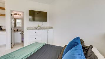 A bedroom with a bed, pillows, a TV, a mirror, and a bathroom visible through an open door.