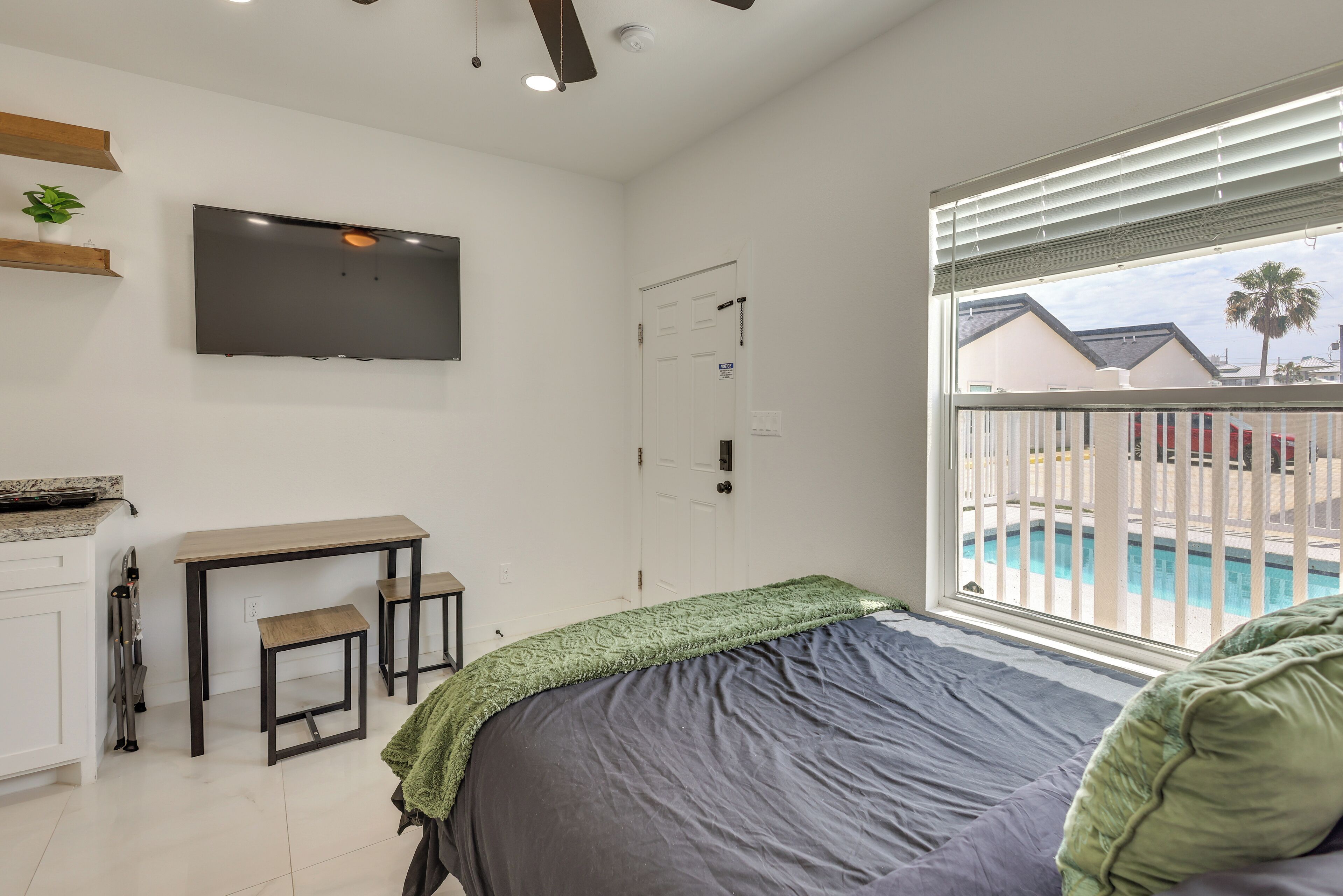A bedroom with a bed, a desk, a TV, and a window with a view of a pool.