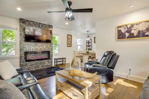 Un salon moderne avec un mur en pierre, un téléviseur à écran plat, une cheminée, des fauteuils en cuir et un coin repas.