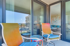 Ein Balkon mit zwei Stühlen, einem kleinen Tisch, einem Sofa und einem Gemälde im Hintergrund.