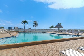 Ein Pool mit Liegestühlen, Palmen und einer Struktur mit Strohdach.