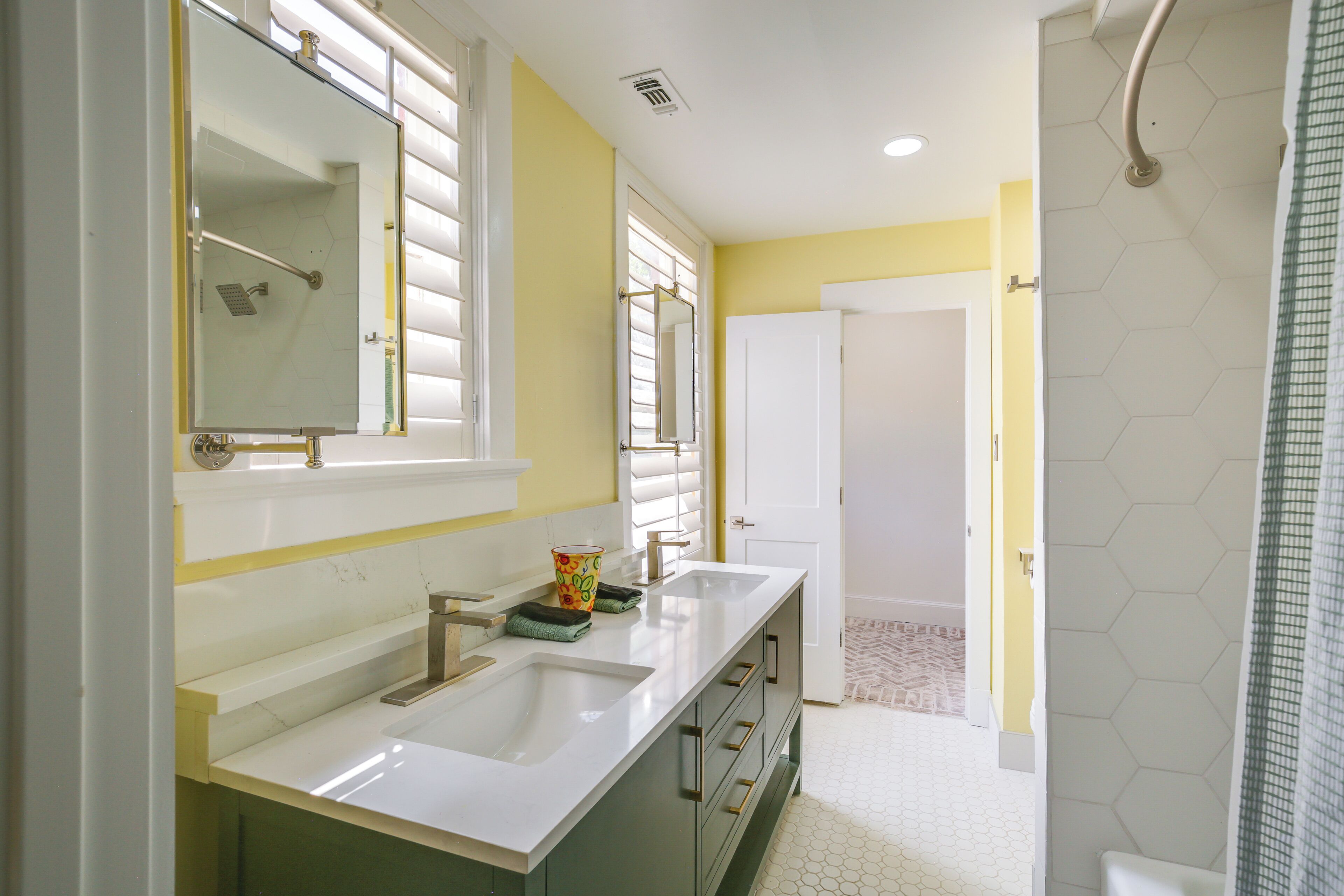 Une salle de bain avec deux lavabos, une douche et une porte donnant sur une autre pièce.