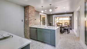 Una cucina con parete decorativa in mattoni, lavastoviglie e zona pranzo con sedie e tavolo.