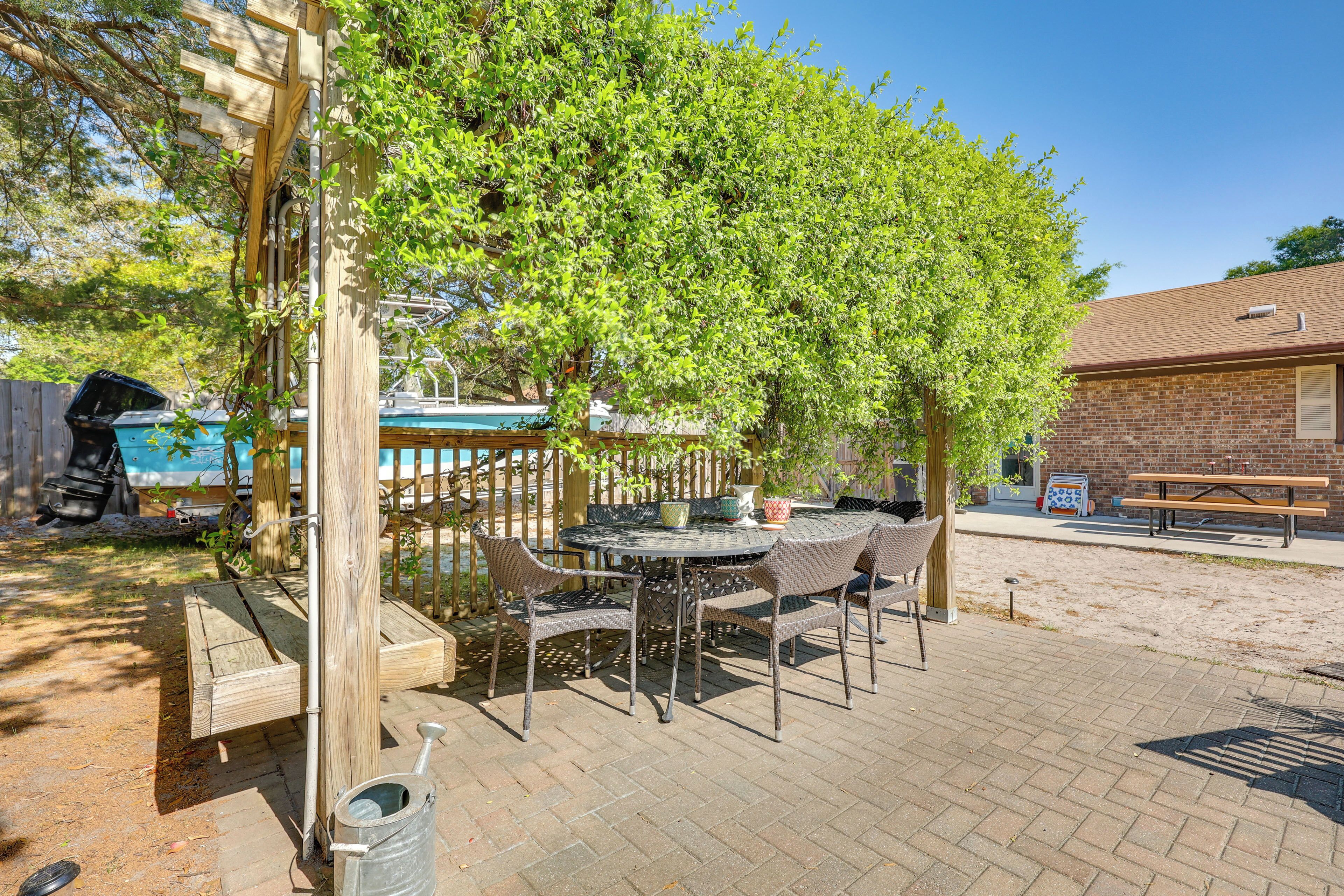 An outdoor patio with a table and chairs, a wooden pergola, and a brick building in the background.