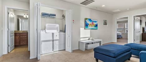 Una habitación con una pared blanca, un banco, un armario blanco y una puerta que da a otra estancia.