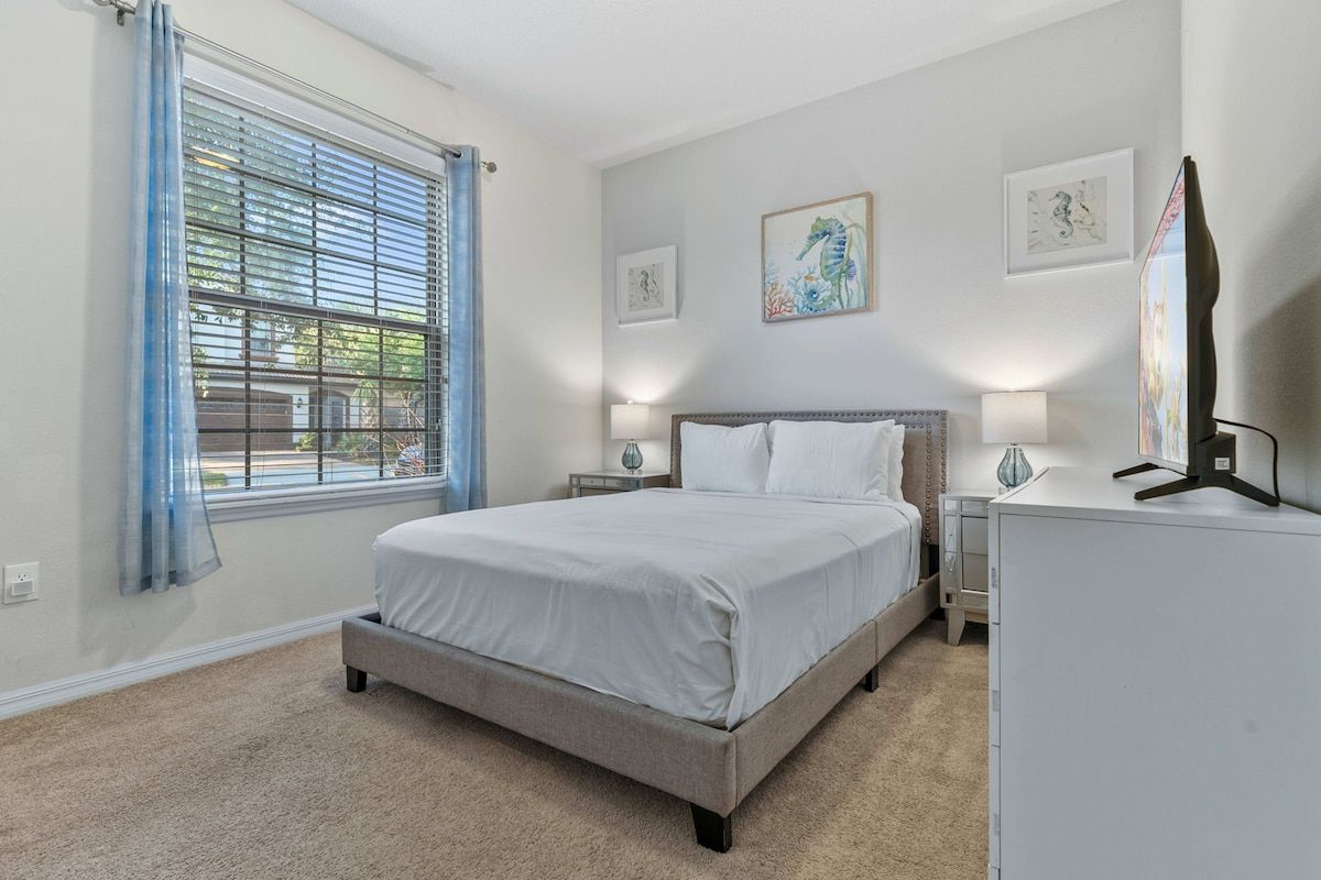A bedroom with a bed, bedside lamps, a dresser, and artwork on the walls.