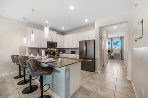 A modern kitchen with white cabinets, a stainless steel refrigerator, and a bar area with stools. - 3BR Condo·Sleeps 12·Free Waterpark·Near Disney (Davenport)