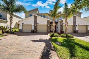 A residential building with multiple garages, a paved driveway, and well-maintained landscaping including palm trees and grass. - 3BR Condo·Sleeps 12·Free Waterpark·Near Disney (Davenport)