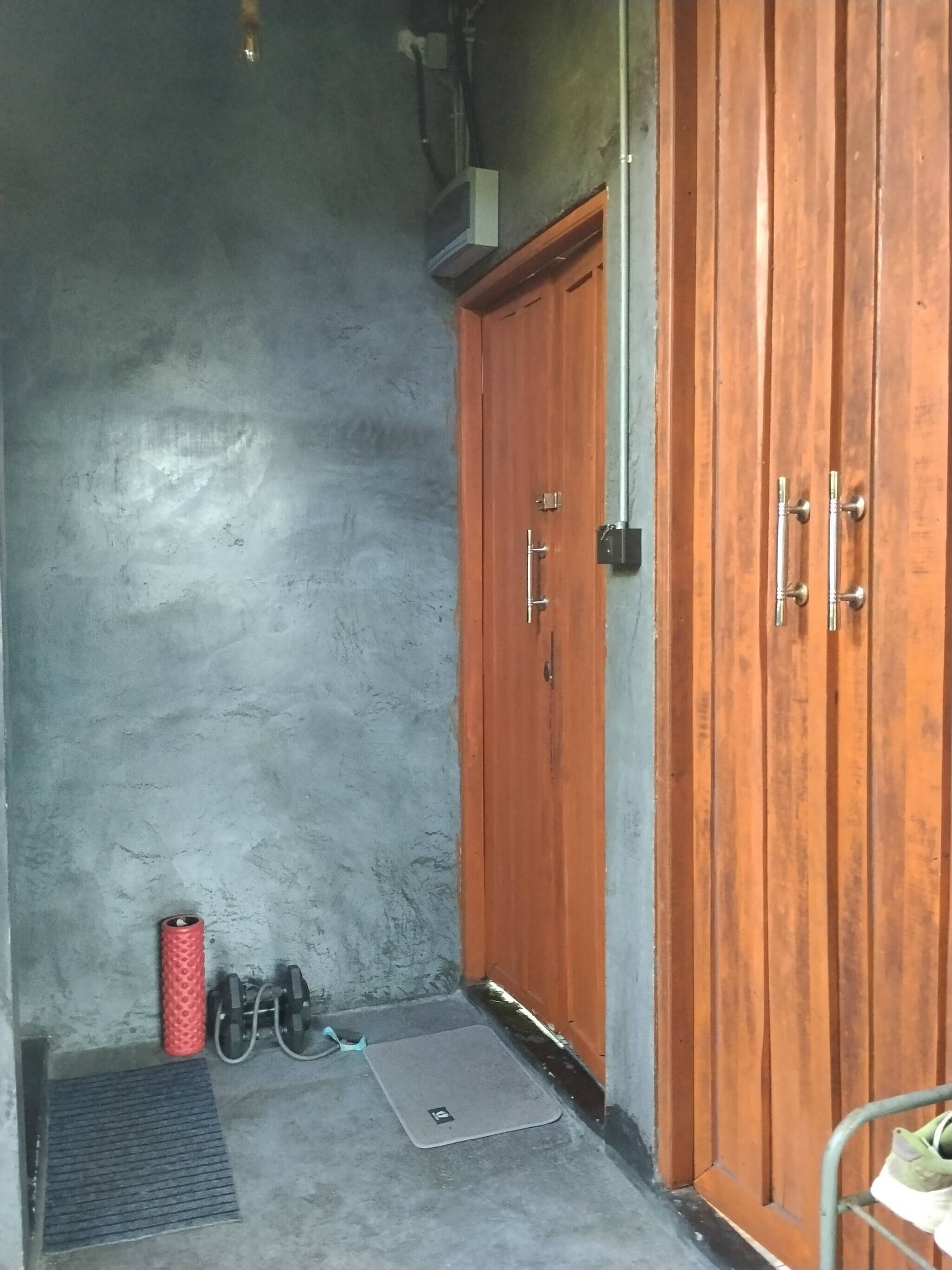 Ein Zimmer mit grauer Wand mit Struktur, einem Holzschrank, einem roten zylindrischen Gegenstand und einer grauen Matte auf dem Boden.