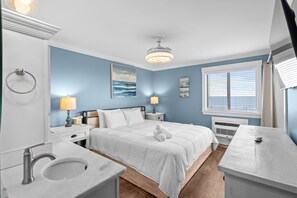 A bedroom with a bed, bedside tables, a window with blinds, a ceiling light, and a wall-mounted air conditioning unit. - Beachfront Bungalow Noon Check In Ocean View Pool (Myrtle Beach)