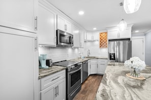 A modern kitchen with white cabinetry, stainless steel appliances, and a marble countertop. - Beachfront Bungalow Noon Check In Ocean View Pool (Myrtle Beach)
