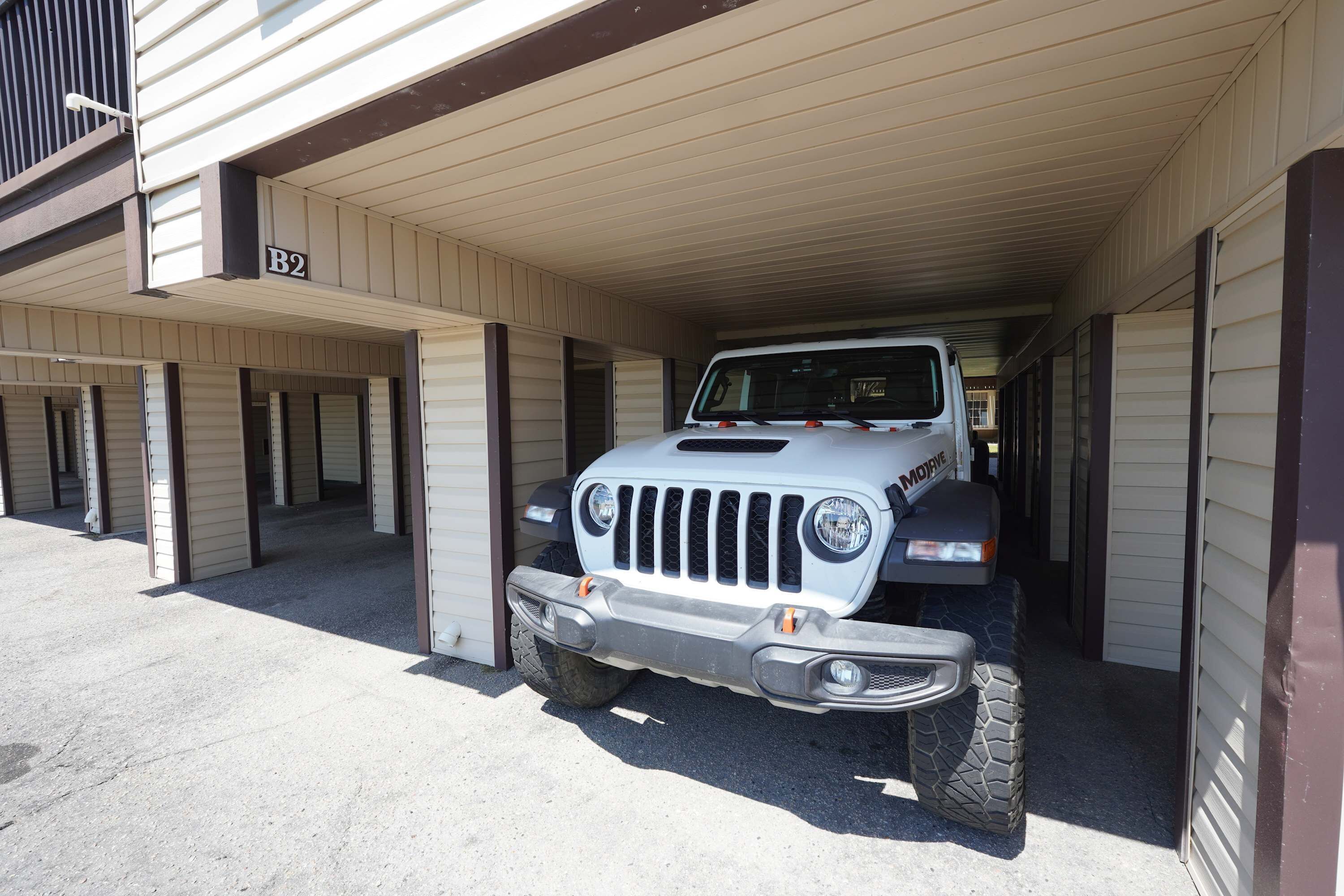 Un veicolo fuoristrada bianco parcheggiato in un'area garage coperta, con un edificio sullo sfondo.