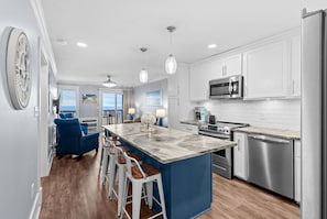 A modern kitchen with white cabinets, stainless steel appliances, and a central island with bar stools. - Beachfront Bungalow Noon Check In Ocean View Pool (Myrtle Beach)