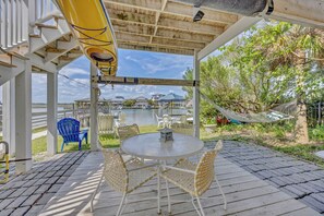 A covered outdoor area with a table and chairs, a hammock, and a view of a body of water and buildings in the background. - The Dolphin House - 4 bedroom soundfront cottage (Wrightsville Beach)