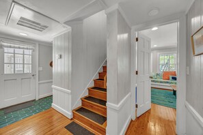 A staircase with white paneling and wooden steps, leading to a room with a window and a colorful rug. - The Dolphin House - 4 bedroom soundfront cottage (Wrightsville Beach)