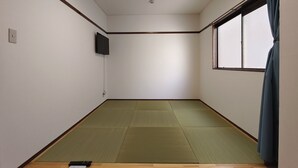 Een kamer met tatami matten, een televisie, een raam met gordijnen en een houten vloer.