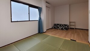 Een kamer met tatami matten, een bank, een raam met gordijnen en een kleine tafel.