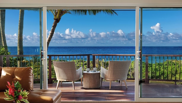 Ein Balkon mit Blick auf den Ozean, zwei Korbstühle, ein kleiner runder Tisch und eine braune Ledersitzbank.