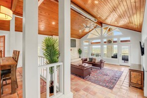 A spacious living area with a high ceiling, large windows, and a view of the outdoors.
