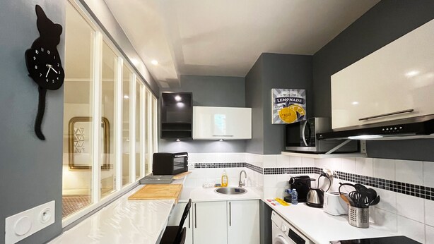 Cocina compacta con lavadora, microondas, fregadero y un reloj en la pared.